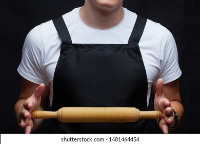 Torso Of A Guy In A Black Apron With A Rolling Pin. Cook, Chef, Butcher, Waiter Or Baker. Place For Text. Copyspace. Mockup.