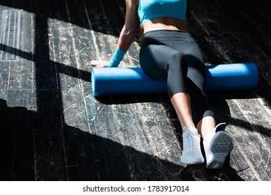 The torso and legs of a slender young woman who goes in for sports in the bright rays of the sun. Working out the fascia of the gluteal muscles with a foam roller.
