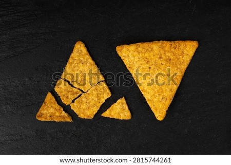 Tortilla chips on black, broken mexican nacho snack, triangle corn chips closeup. Hot crunchy totopos, spicy tortilla chips
