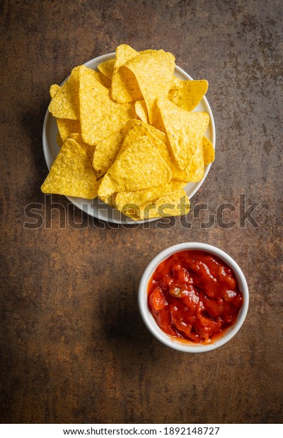 Tortilla chips and red tomato salsa dip.\
Mexican nacho chips on brown table. Top\
view.