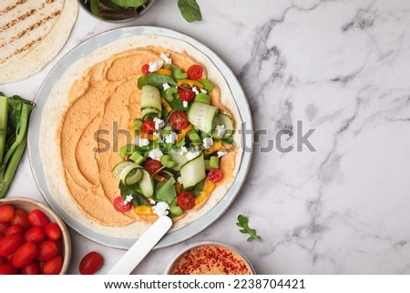 Tortilla with hummus and vegetables on white marble table, flat lay. Space for text