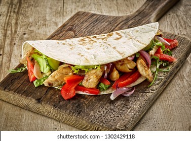Tortilla wrap with fried chicken meat and vegetables on wooden table