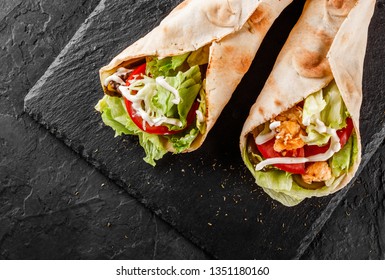 Tortilla wraps with grilled chicken, fresh vegetables and salad on black stone background. Healthy snack or take-away lunch. Top view, flat lay - Powered by Shutterstock