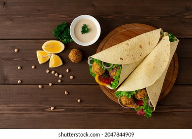 Tortillas wrapped with falafel balls and fresh vegetables, vegetarian healthy food, on a wooden background, no people,