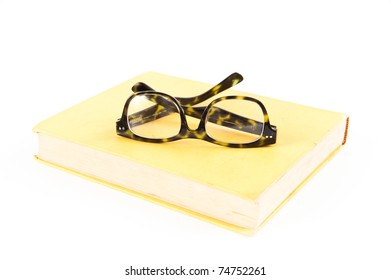 Tortoise Shell Glasses On Yellow Book Isolated On White