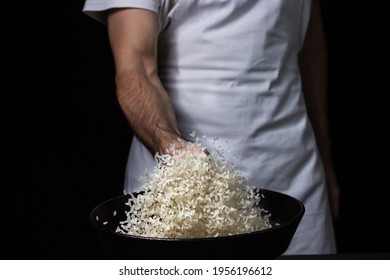 Toss The Rice In The Skillet. The Cook Is Throwing Rice On A Black Background. Cooking. Photo Of Food On A Dark Background