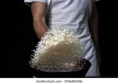 Toss The Rice In The Skillet. The Cook Is Throwing Rice On A Black Background. Cooking. Photo Of Food On A Dark Background