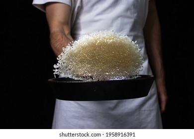 Toss The Rice In The Skillet. The Cook Is Throwing Rice On A Black Background. Cooking. Photo Of Food On A Dark Background