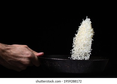 Toss The Rice In The Skillet. The Cook Is Throwing Rice On A Black Background. Cooking. Photo Of Food On A Dark Background