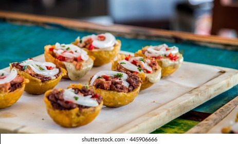 Tostones cup, Crushed fried plantains with beans, onion, tomato and white cheese on green table.