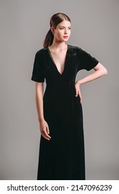 Total black look. Black velours trumpet dress. Evening floor length gown with deep v neck line and short sleeves. Beautiful young brunette lady with red lips posing in studio. Femme fatale