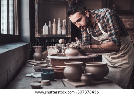 Total concentration at work. Confident young man making ceramic pot on the pottery wheel