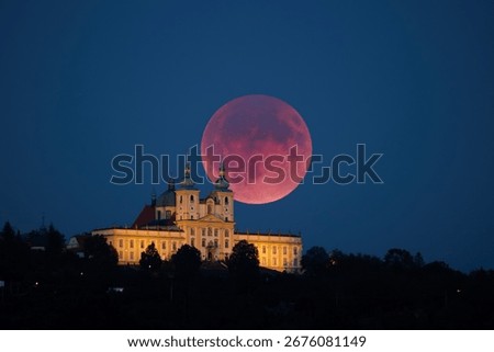 Total lunar eclipse with a glowing red moon rising above the illuminated baroque Pilgrimage Basilica of Our Lady of the Holy Hill. Blood moon rising over baroque church in Olomouc, Czech republic.