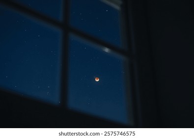 A total lunar eclipse viewed through a window.