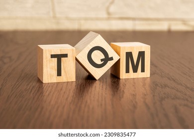 total quality management concept with symbols TQM on wooden cubes, dark wooden background - Shutterstock ID 2309835477