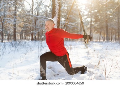 Total resistance fitness. Active mature sportsman working out with TRX system outside, training with suspension straps in winter park. Fit senior male doing strength and flexibility exercises outdoors