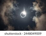 Total solar eclipse of April 8th 2024 with the sun peaking from behind the moon creating. a diamond ring effect. Totality with bright corona visible against dark blue sky with a few clouds