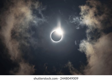 Total solar eclipse of April 8th 2024 with the sun peaking from behind the moon creating. a diamond ring effect. Totality with bright corona visible against dark blue sky with a few clouds - Powered by Shutterstock