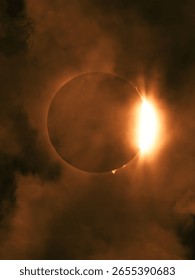 Total solar eclipse with bright flare and cloudy sky atmosphere.