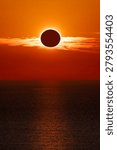 Total solar eclipse at sunset over the ocean, with a spectacular orange sky and the sun