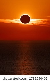 Total solar eclipse at sunset over the ocean, with a spectacular orange sky and the sun's reflection on the water.