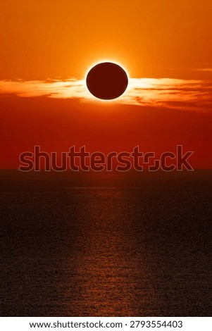 Total solar eclipse at sunset over the ocean, with a spectacular orange sky and the sun's reflection on the water.