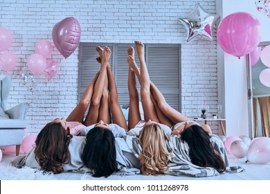 Totally carefree. Playful young women keeping feet up while lying on the bed