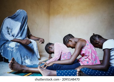 Totally covered person holding a blade speaking to a group of intimidated black African girls sitting in a row on the floor with their heads bowed prior to the female genital mutilation intervention - Shutterstock ID 2095148470