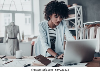 In touch with clients. Beautiful young African woman working using computer while standing in workshop  - Powered by Shutterstock