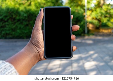 Touch Screen Mobile Phone, In African Woman's Hand. Black Female Holding Smart Phone On Green Outdoor Background With Blank Copy Space Screen For Your Text Message Or Information Content