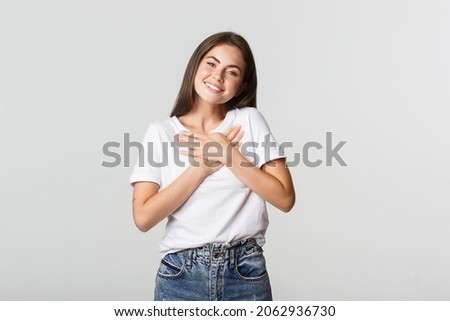 Touched happy young woman smiling, holding hands on chest, feeling thankful