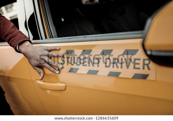 Touching car. Close up of instructor\
touching bright orange student driver car standing\
outside