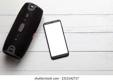 Touchscreen Smartphone And Wireless Portable Bluetooth Speaker On A Wooden Board, Top View.