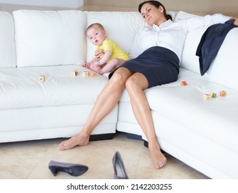 Its Tough Being A Working Mom. Exhausted Young Working Mother Asleep On The Couch Next To Her Baby.