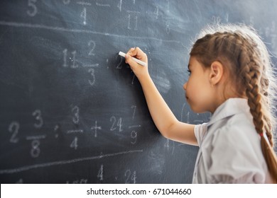 Tough Day At School! Cute Child Near The Blackboard Indoors. Kid Is Learning In Class. Complex Math, Arithmetic And Examples. Numbers Written With Chalk On Board.
