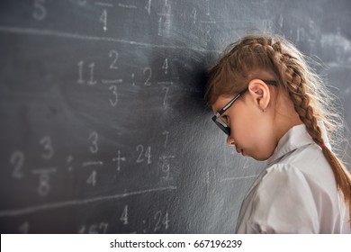 Tough day at school! Sad child near the blackboard indoors. Kid is learning in class. Complex math, arithmetic and examples. Numbers written with chalk on board.