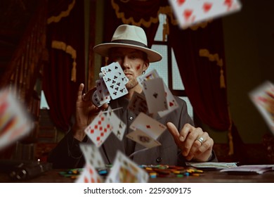 A tough gangster man in an elegant black suit and a white hat sits in a luxury apartment and plays cards. Retro style. Detective movie. The criminal world of the mafia. 