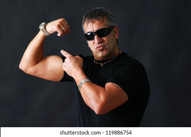 Tough Guy With Dark Glasses, Could Be Criminal, Showing His Big Bicep Muscle Has An Intimidation Tactic, Studio Shot Over Black.