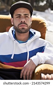 A Tough Guy In A Tough Neighborhood. Portrait Of A Serious Man Sitting On A Couch In The Outdoors.