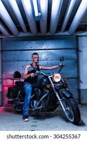 Tough Guy With Sparrow Beard, Undercut And Blue Jeans Sitting On A Chopper Motorcycle In An Underground Car Park. Neon Look.