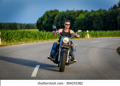 Tough Guy With Sparrow Beard, Undercut And Blue Jeans In Motion On The Road On A Chopper Bike