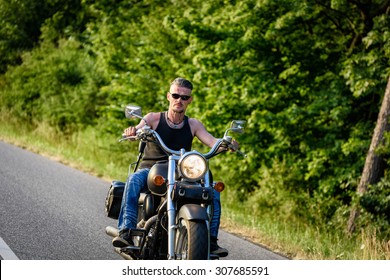 Tough Guy With Sparrow Beard, Undercut And Blue Jeans In Motion On The Road On A Chopper Bike