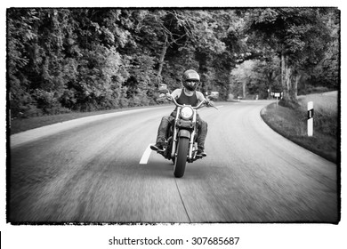 Tough Guy With Sparrow Beard, Undercut And Blue Jeans In Motion On The Road On A Chopper Bike