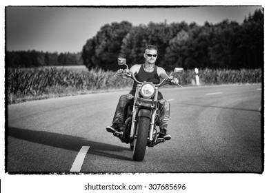 Tough Guy With Sparrow Beard, Undercut And Blue Jeans In Motion On The Road On A Chopper Bike