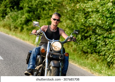 Tough Guy With Sparrow Beard, Undercut And Blue Jeans In Motion On The Road On A Chopper Bike