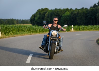 Tough Guy With Sparrow Beard, Undercut And Blue Jeans In Motion On The Road On A Chopper Bike