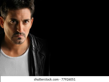 Tough looking man wearing black leather jacket against black background with lots of copy space