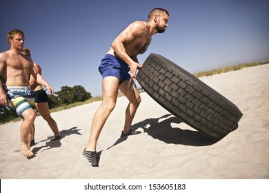 Tough male athlete flipping a truck tire. Young people doing  exercise on beach. - Powered by Shutterstock