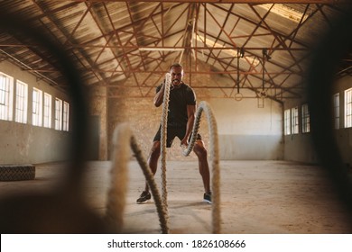 Tough man working out in training gym made inside old factory. Fitness man exercising with battle rope in abandoned warehouse. - Powered by Shutterstock