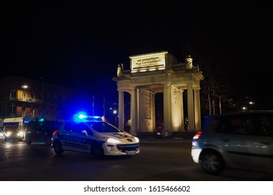 Toulouse, France - Dec. 2017 - Photo With Blur Motion Of A Police Car Responding By Night, With Blue Rotating Lights On, In Front Of The Illuminated War Memorial Arch Of François Verdier Street